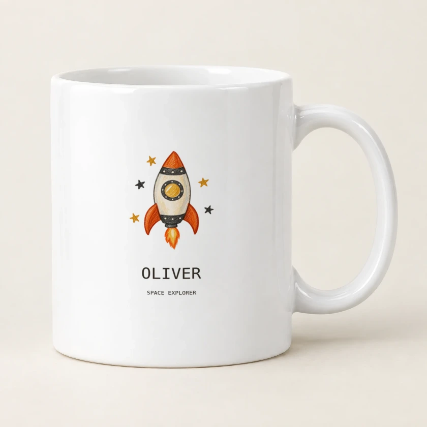 White ceramic mug printed with an orange rocket drawing and OLIVER beneath